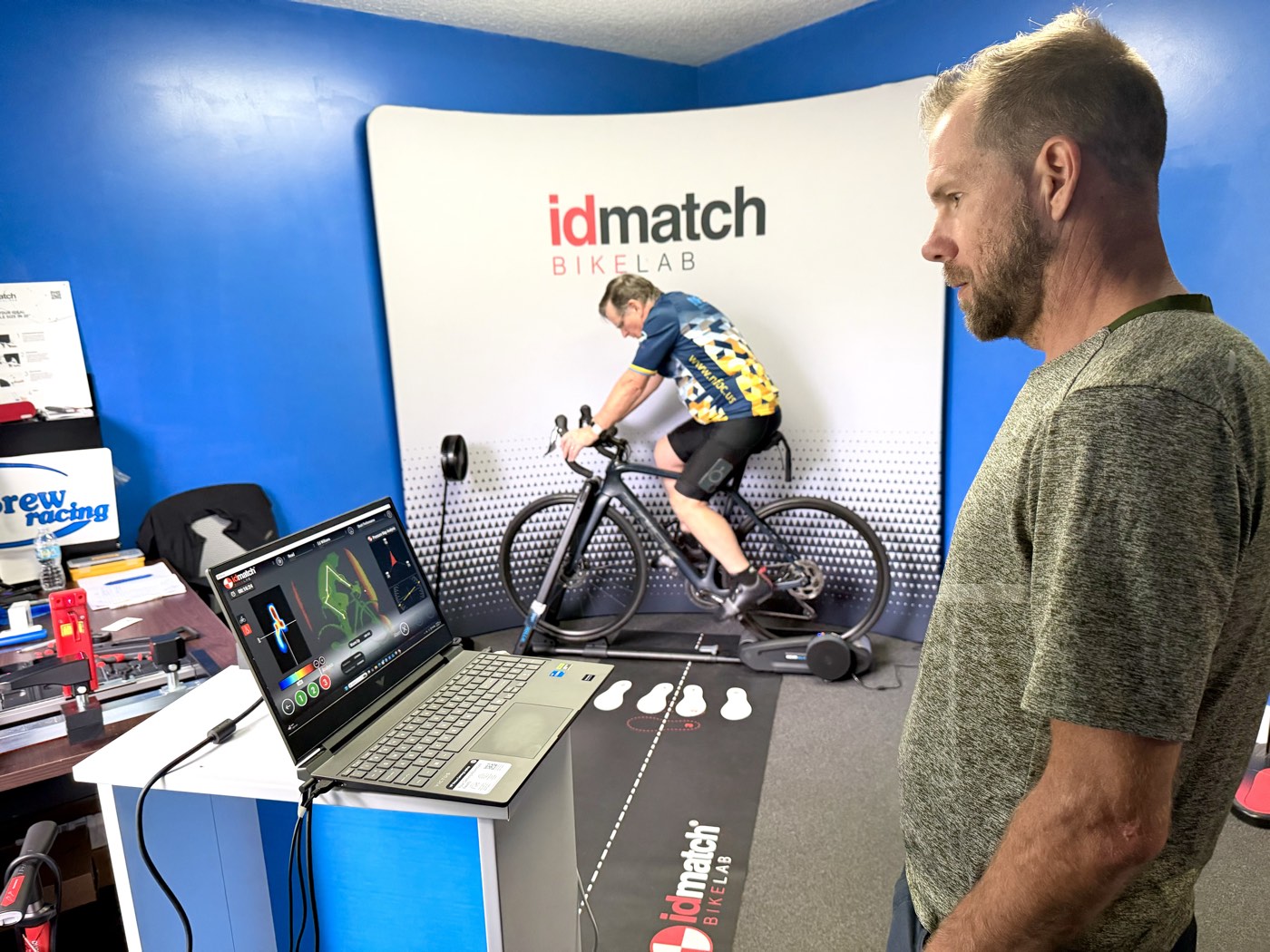 Shott Performance IDmatch bike fitting studio in Jacksonville — a rider pedaling on a trainer in the IDmatch BIKELAB while a fitter reviews live data on a laptop.
