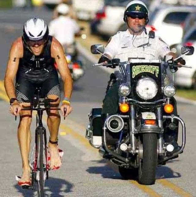 A cyclist on the IRONMAN Jacksonville bike course with a sheriff motorcycle escort
