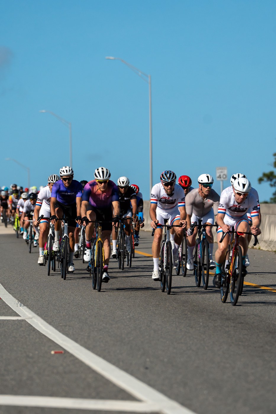 A large group of cyclists riding together up a bridge under clear blue sky during a Jax Sub 4 century.