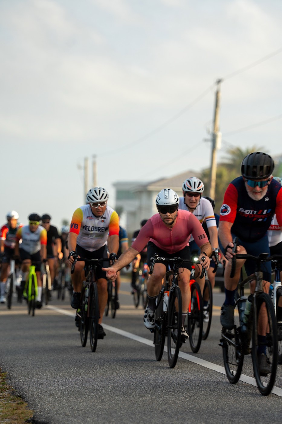 Riders packed into a tight group on a coastal road, one in Shott Performance kit, during a Jax Sub 4 century.